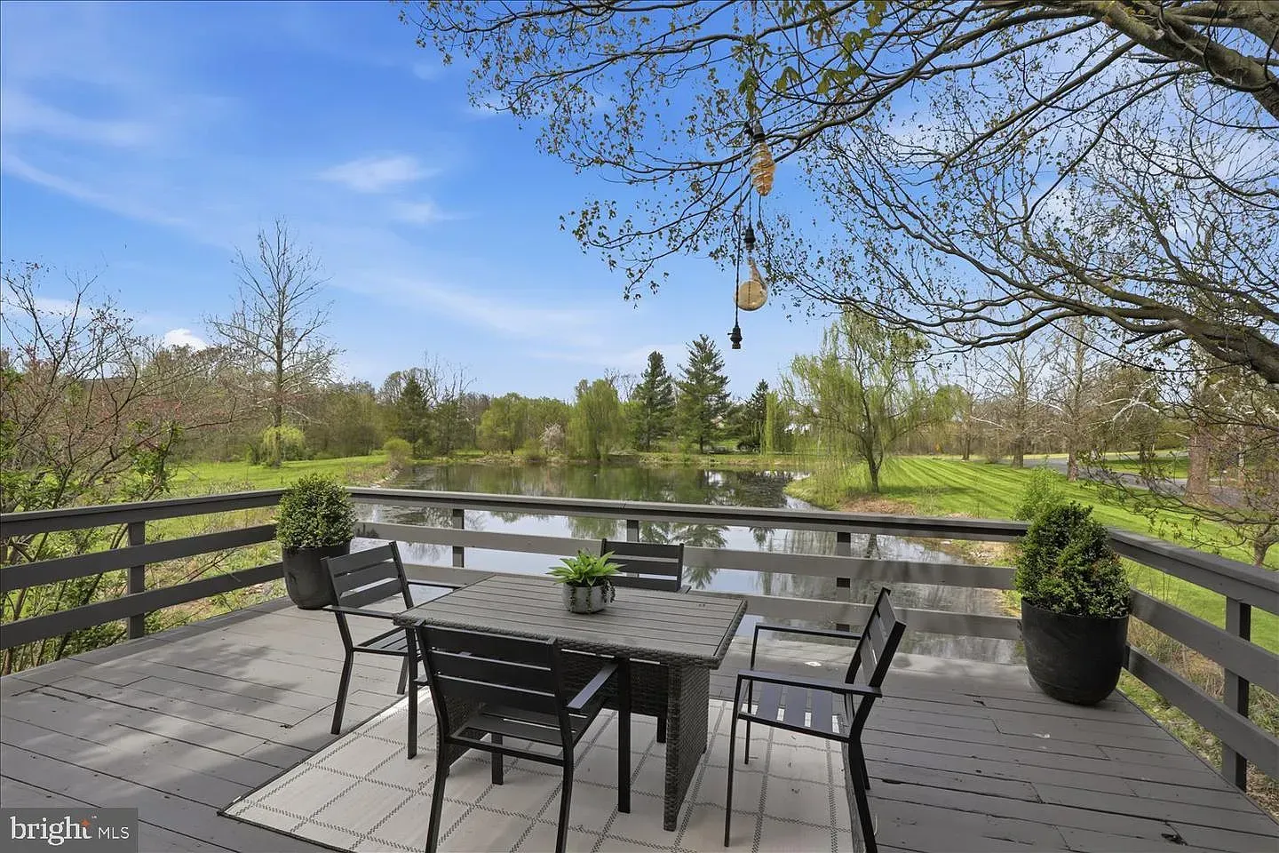 Patio deck with table and chairs overlooking a pond and trees under a blue sky