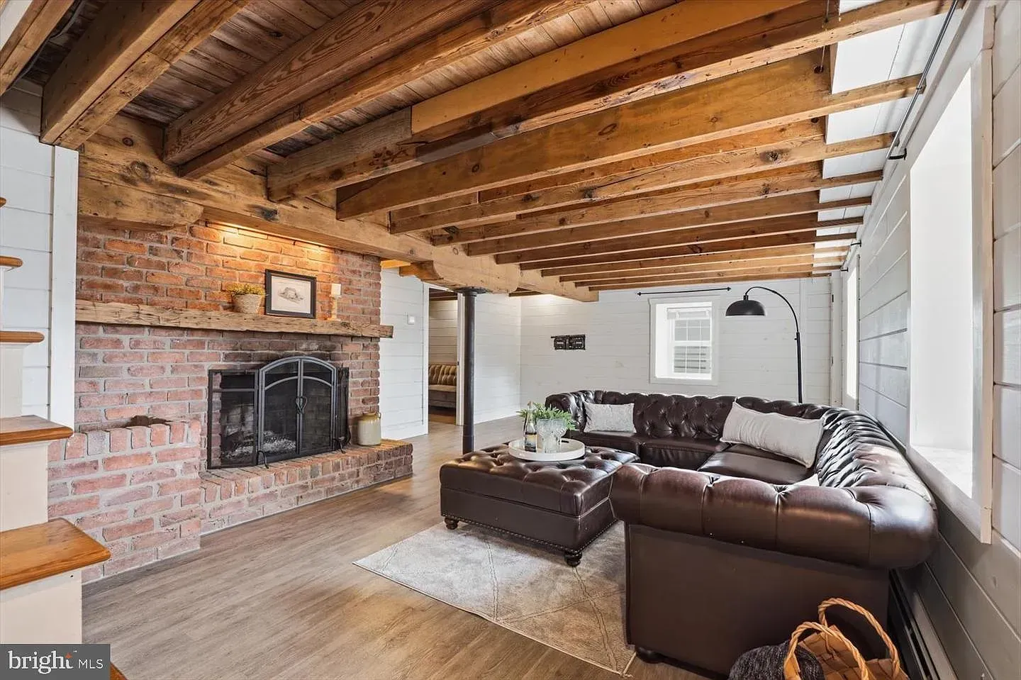 Cozy living room with exposed wood beam ceiling, brick fireplace, and brown sectional sofa