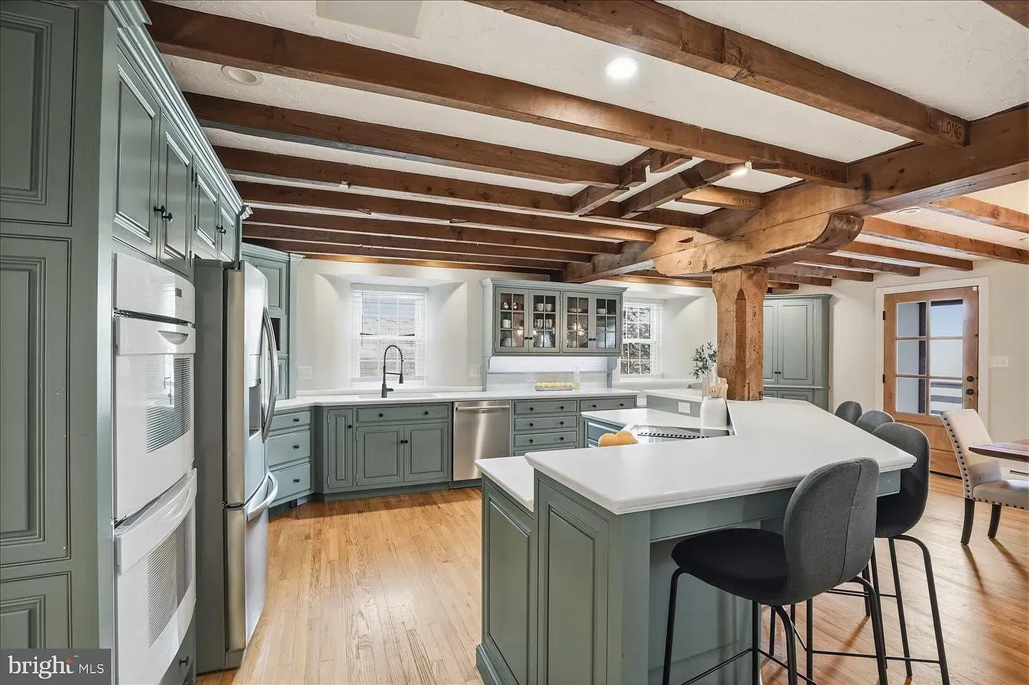 Bright kitchen with green cabinets, white island, wood beams, and barstools in a modern home