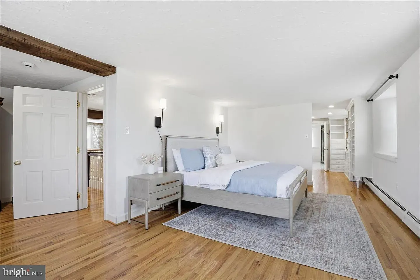 Bright bedroom with a gray bed, white walls, wood floors, and a gray rug.