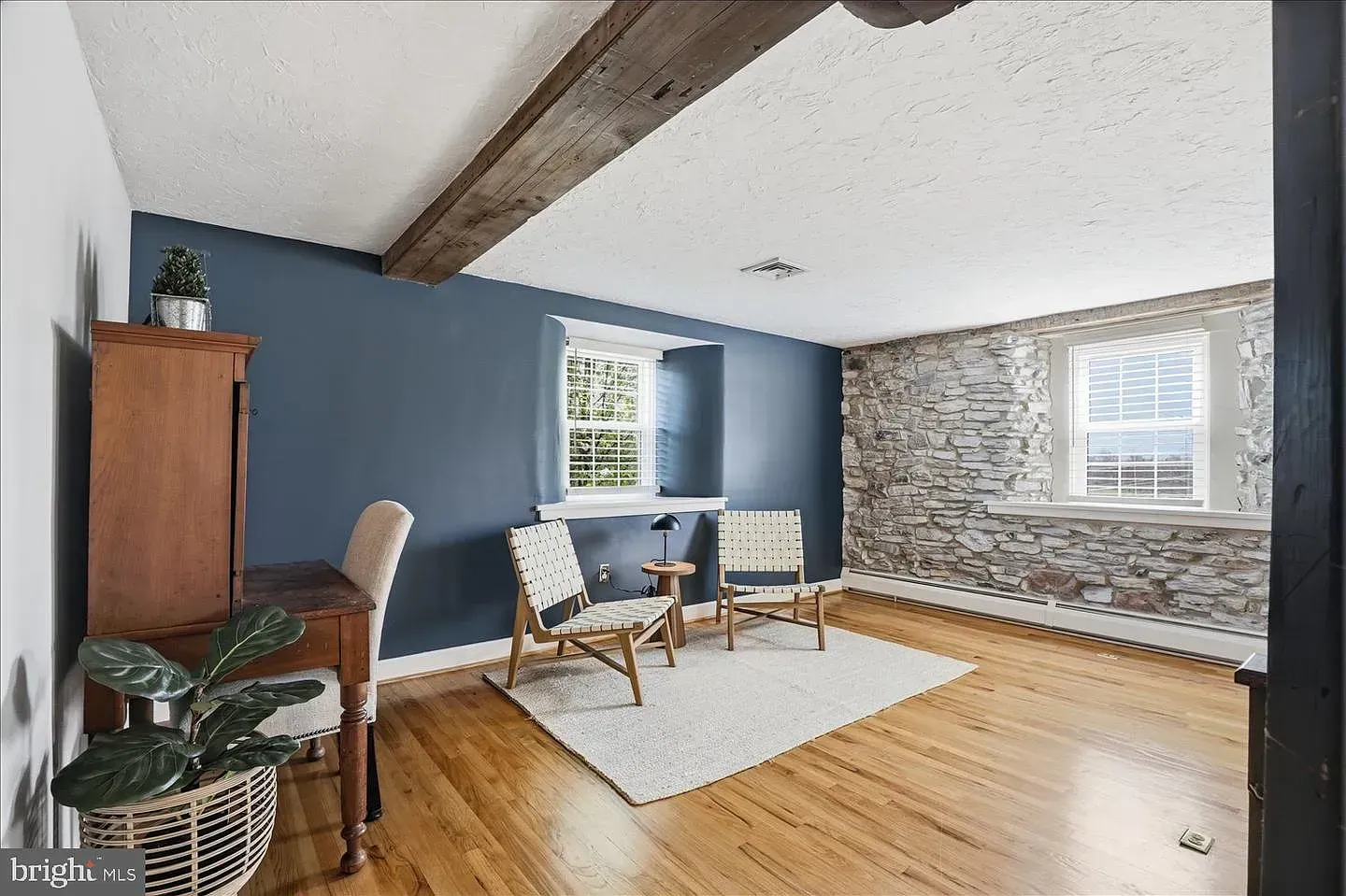 Cozy living room with blue walls, wood floors, stone accent wall, and desk by a window.