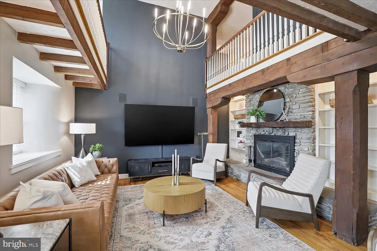 Bright living room with exposed beams, large TV, stone fireplace, and neutral seating area