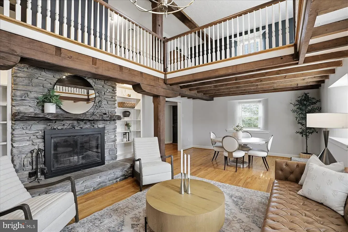 Modern living room with stone fireplace, loft balcony, and neutral seating around a round coffee table
