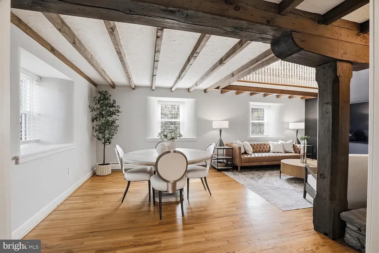 Bright open dining and living room with white walls, wood beams, hardwood floors, and modern furniture