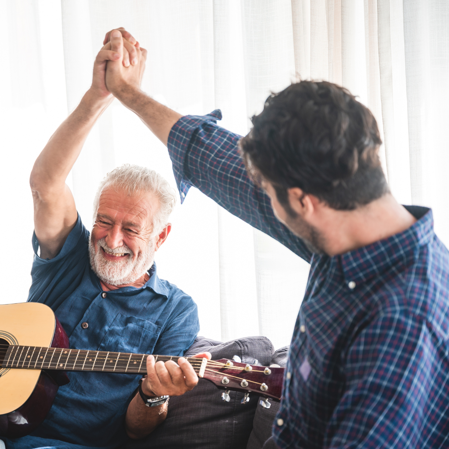 old man playing guitar, high-fiving younger man