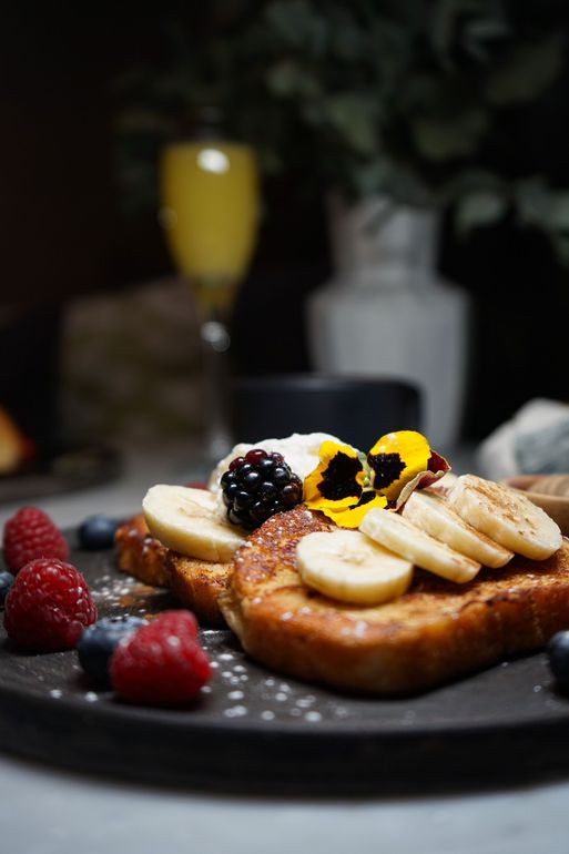 French toast with bananas , raspberries and blueberries on a plate.