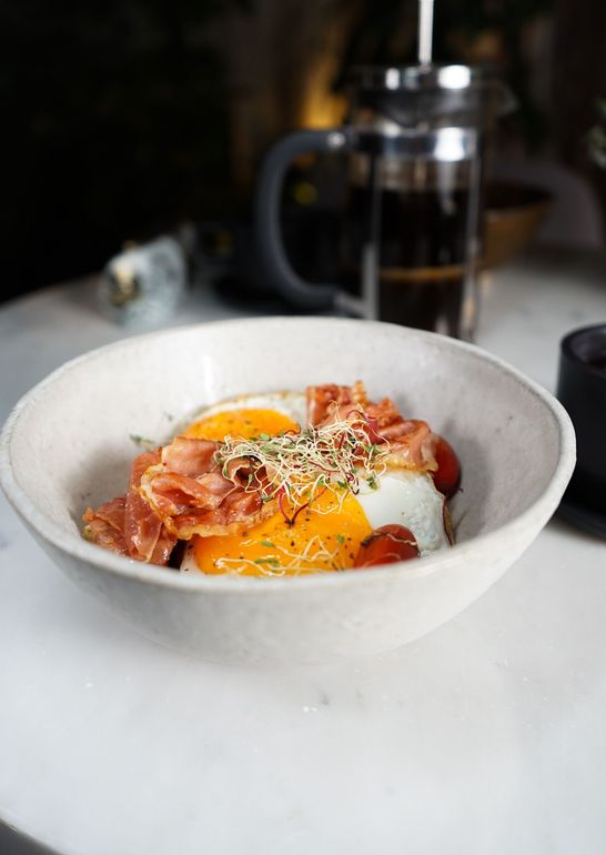 A bowl of food with eggs , bacon and tomatoes on a table.