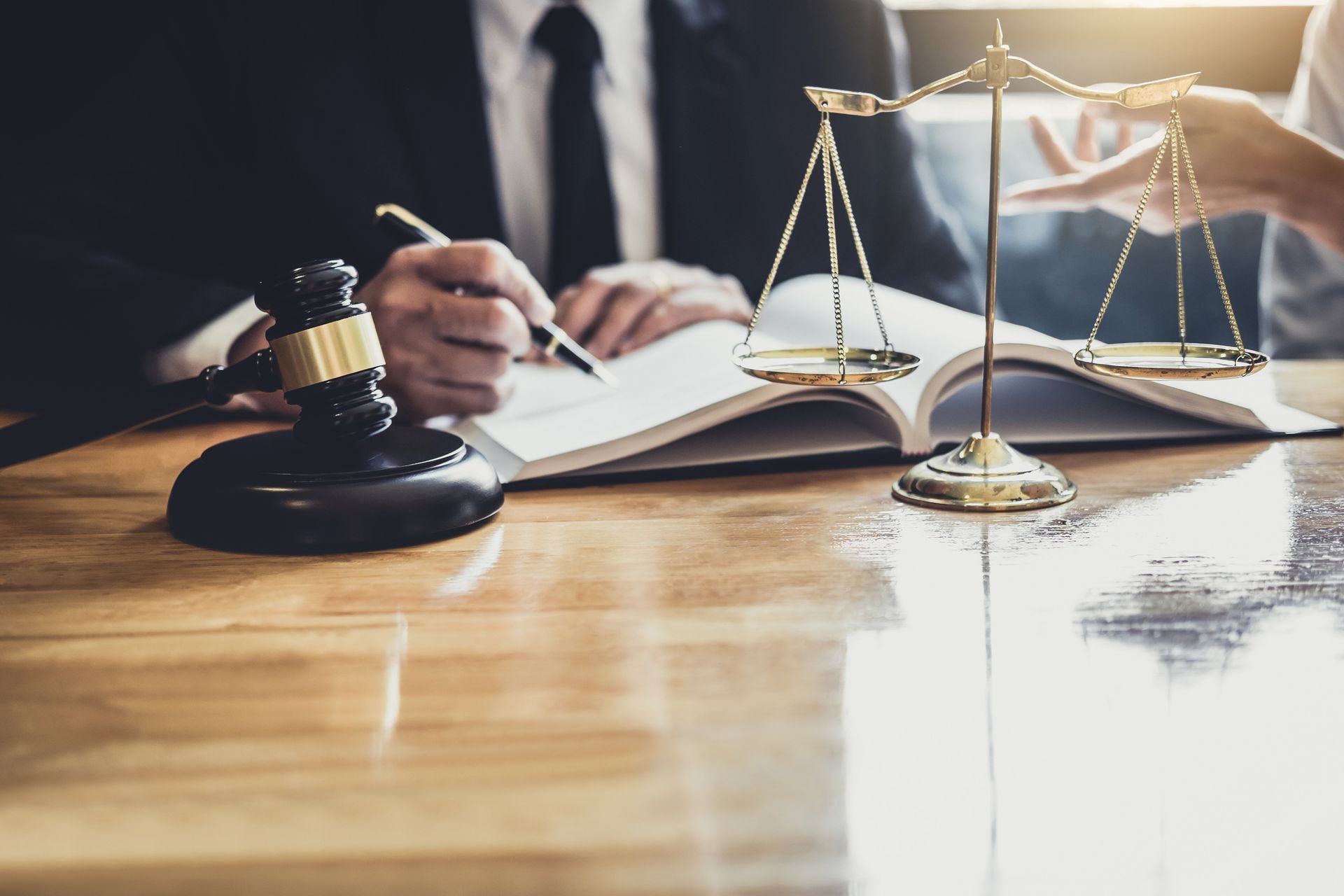 Lawyer and client consult, with gavel, scales of justice, and legal documents on a wooden table.