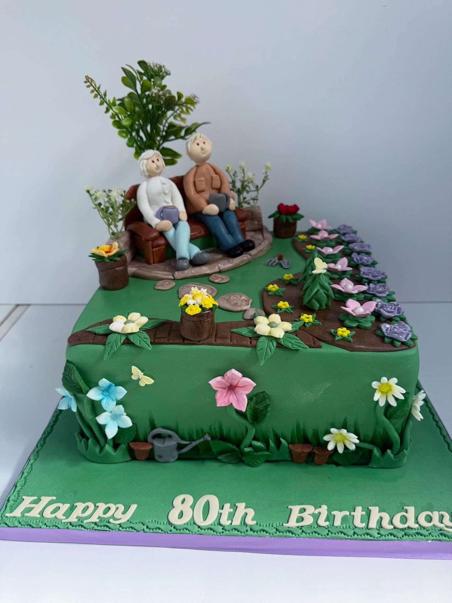 Decorative 80th birthday cake with fondant figures of an elderly couple sitting on a bench