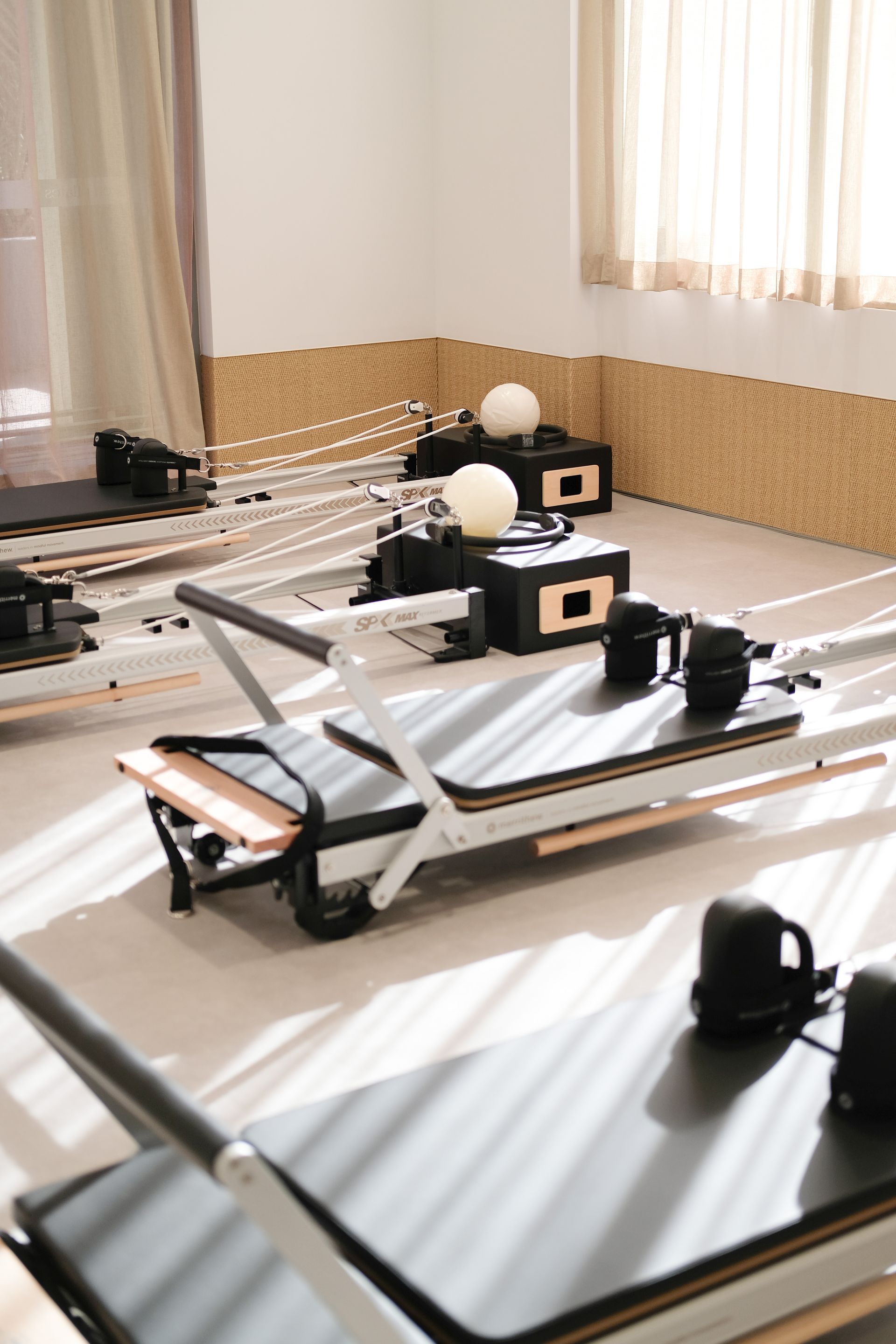 Row of massage tables in a sunlit treatment room with white sheets and folded black towels