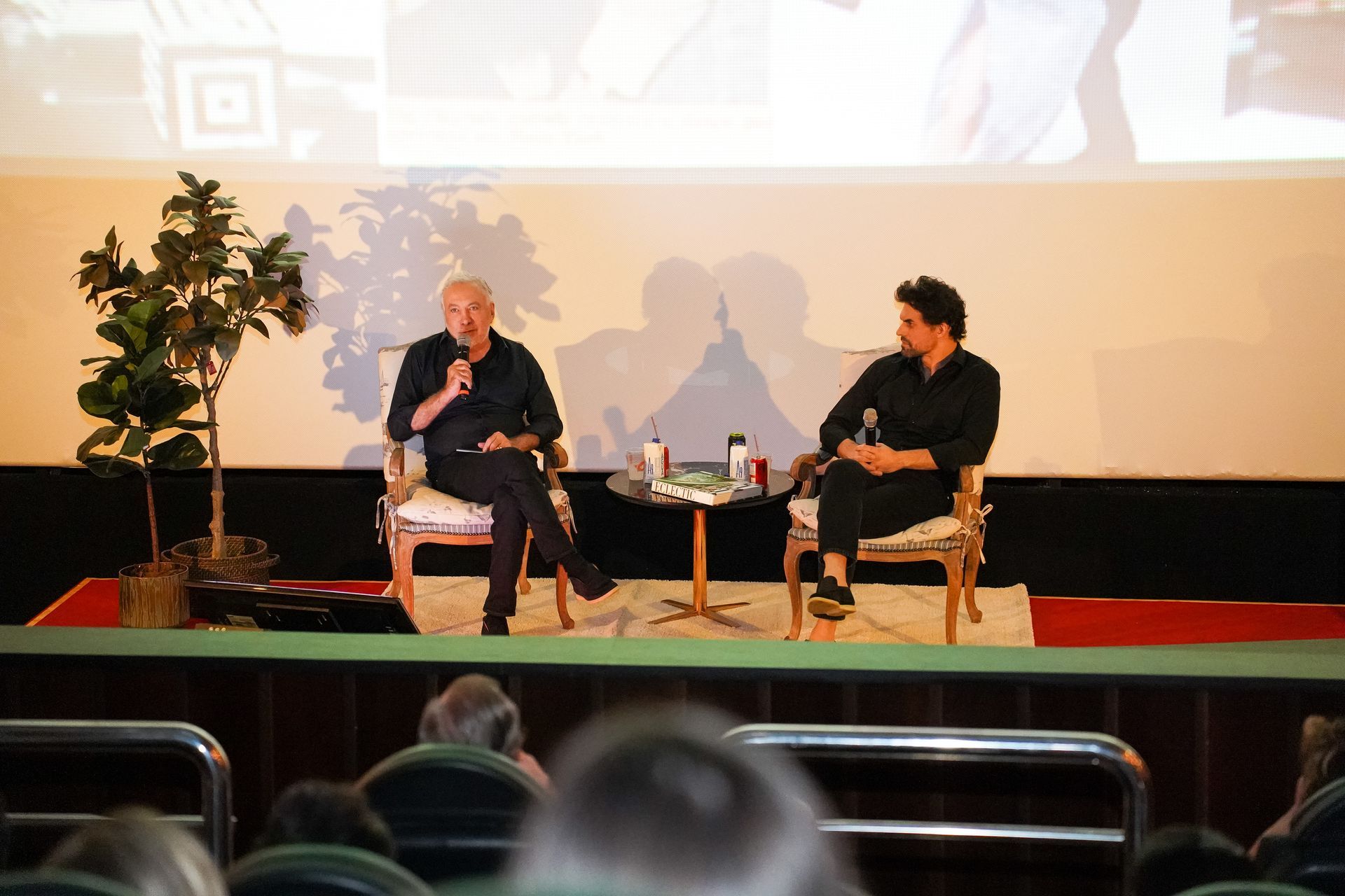 Um homem está sentado em um sofá ao lado de um vaso de flores.