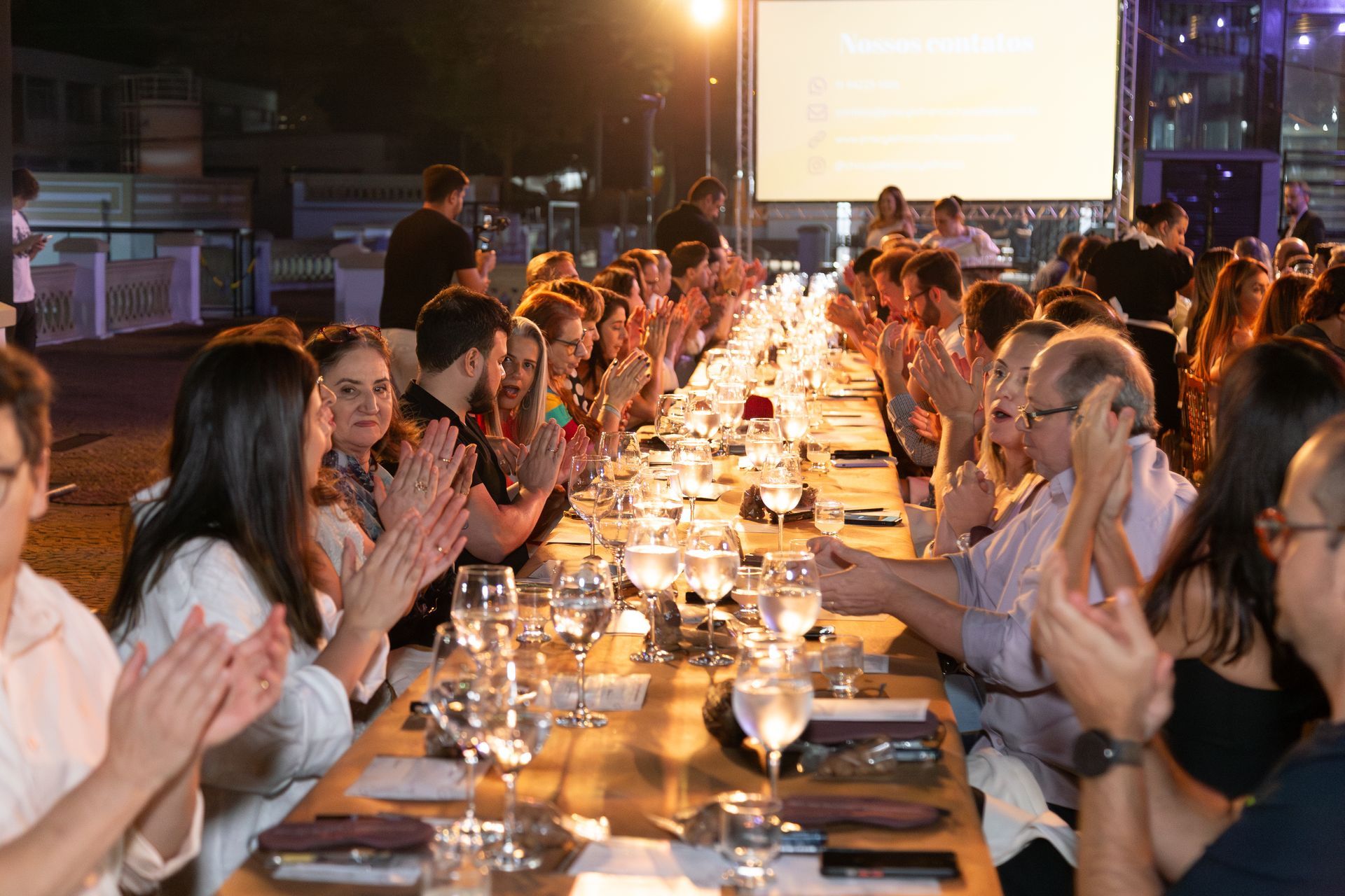 Um grupo de pessoas está sentado em uma mesa longa batendo palmas