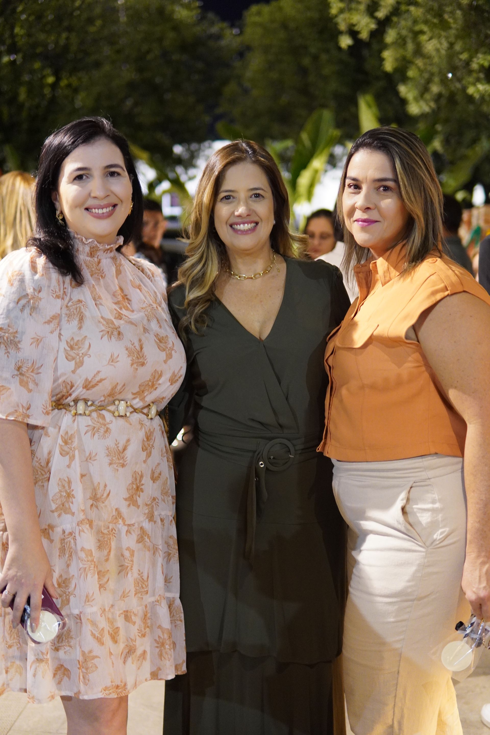 Três mulheres estão posando para uma foto juntas em um parque.