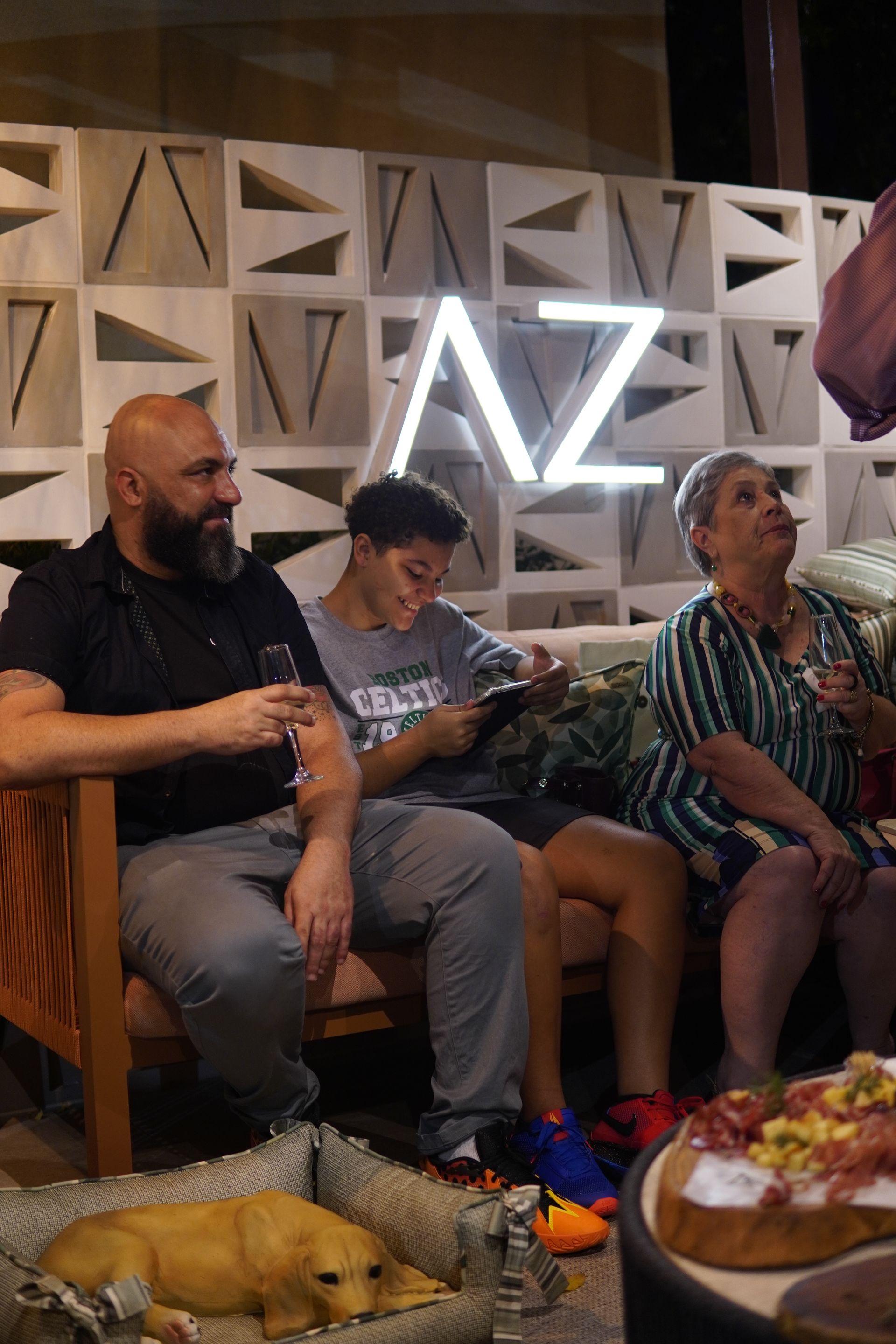 Um grupo de pessoas está sentado em um sofá com um cachorro em uma cama de cachorro.