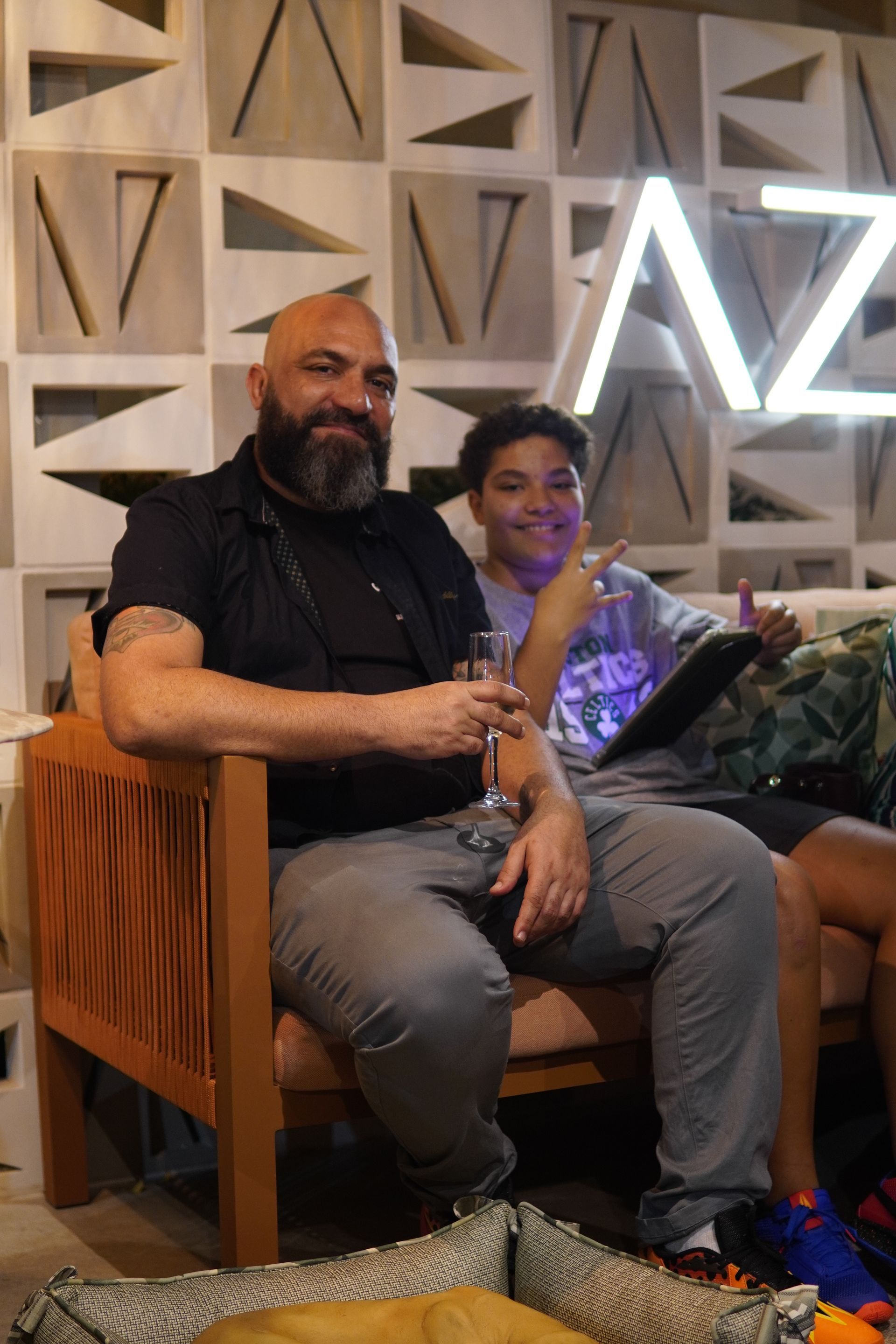 Um homem e um menino estão sentados em uma cadeira bebendo vinho.