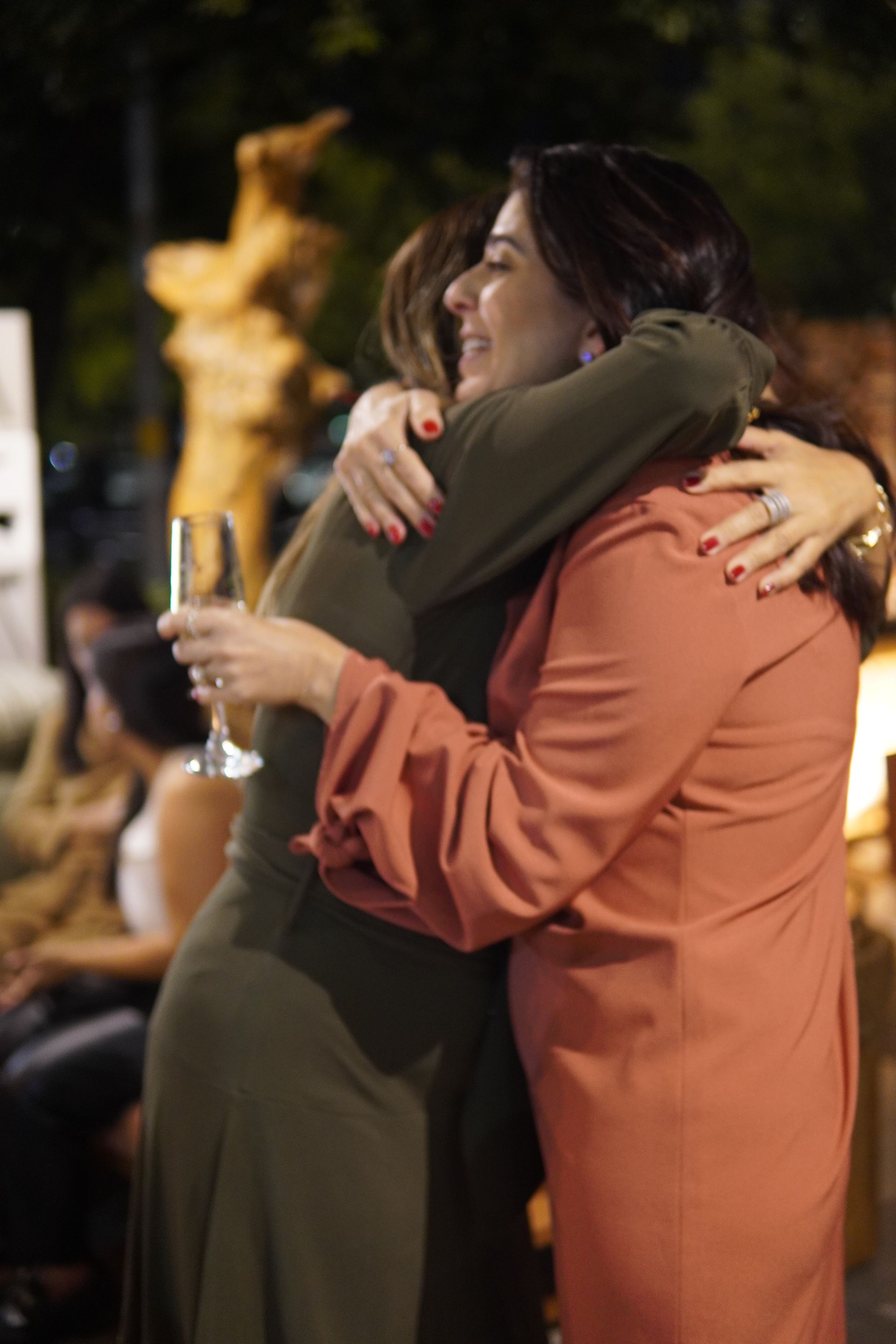 Duas mulheres estão se abraçando enquanto seguram uma taça de vinho.