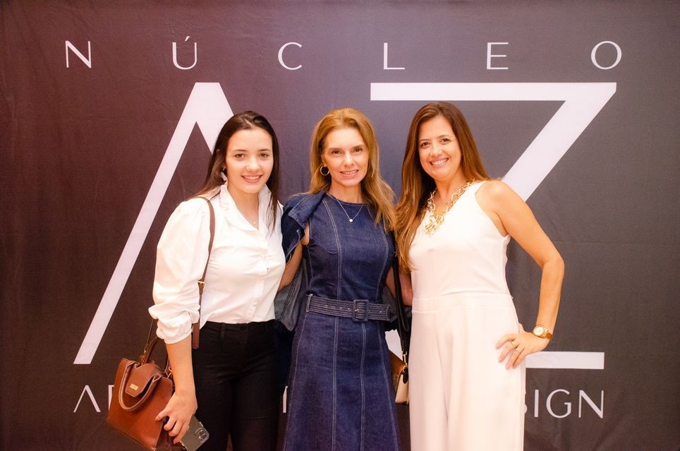 Três mulheres estão posando para uma foto em frente a uma placa que diz nucleo