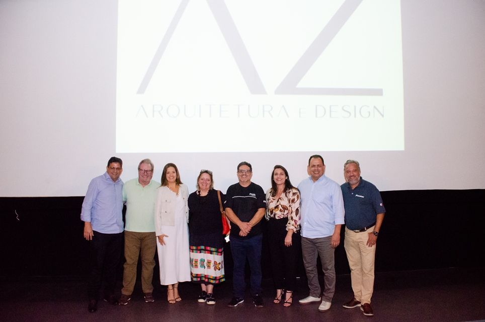 Um grupo de pessoas está posando para uma foto em frente a uma tela de projeção.