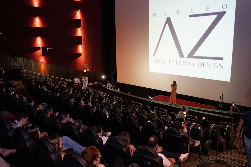 Um grande grupo de pessoas está sentado em um auditório assistindo a uma apresentação do núcleo