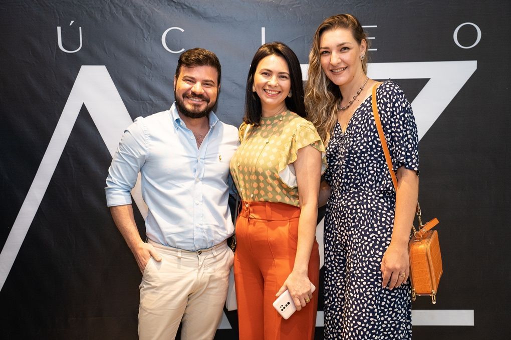 Um homem e duas mulheres estão posando para uma foto em frente a uma placa.