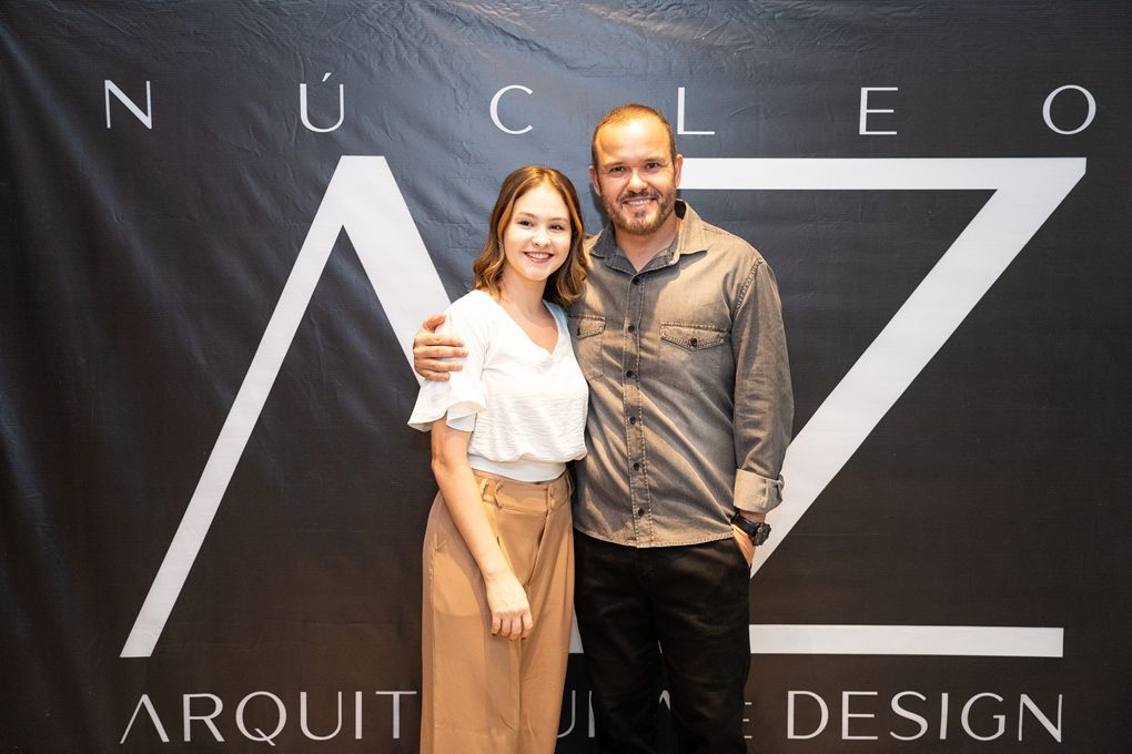 Um homem e uma mulher estão posando para uma foto em frente a uma placa que diz nucleo