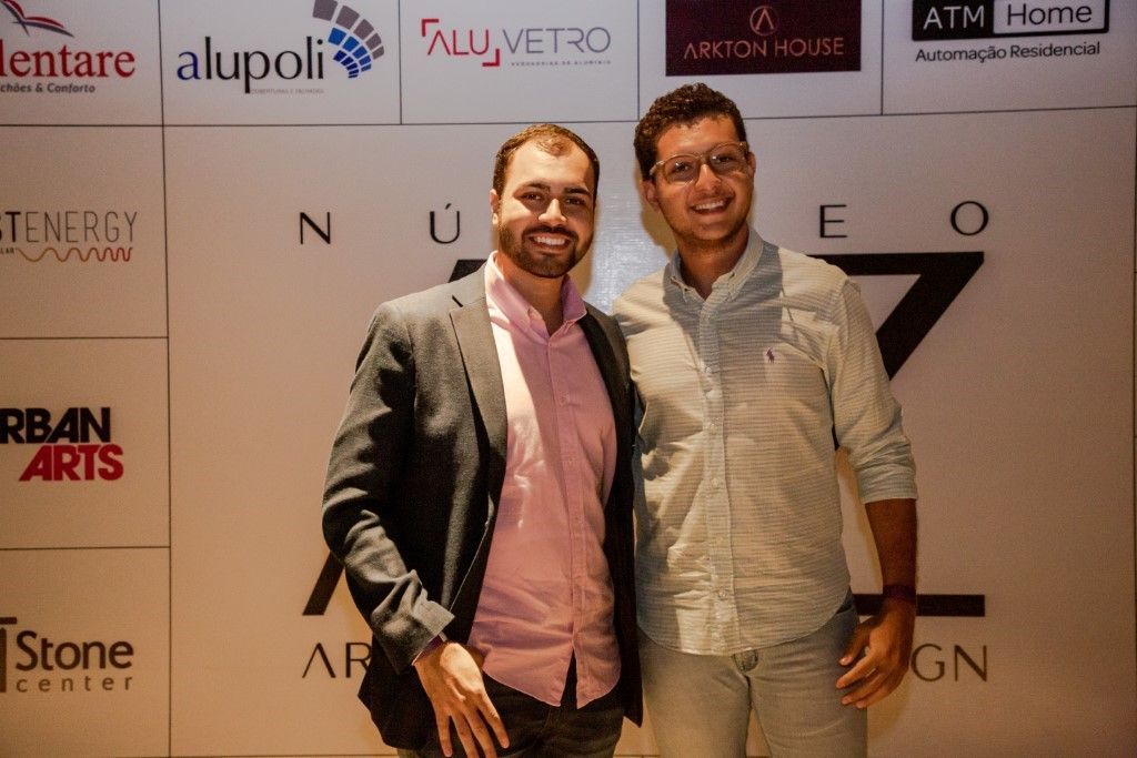 Dois homens estão posando para uma foto em frente a uma parede com logotipos.