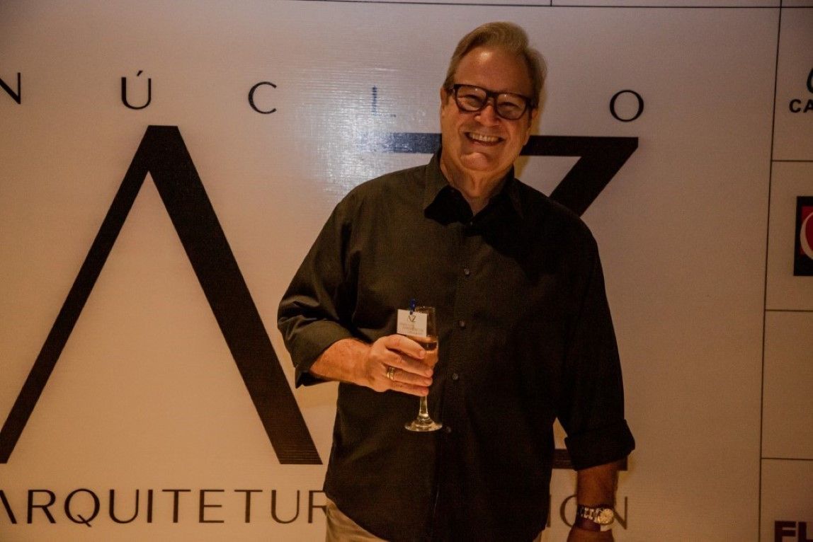 Um homem segura uma taça de vinho em frente a uma placa que diz arquitetur