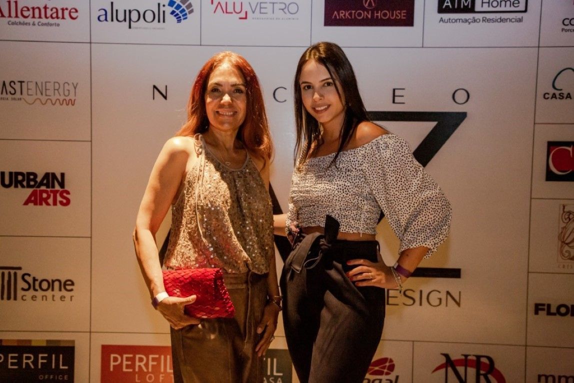 Duas mulheres estão posando para uma foto em frente a uma parede com logotipos.