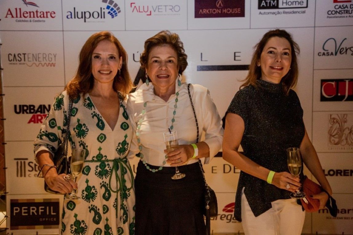 Três mulheres estão posando para uma foto em frente a uma parede com logotipos.