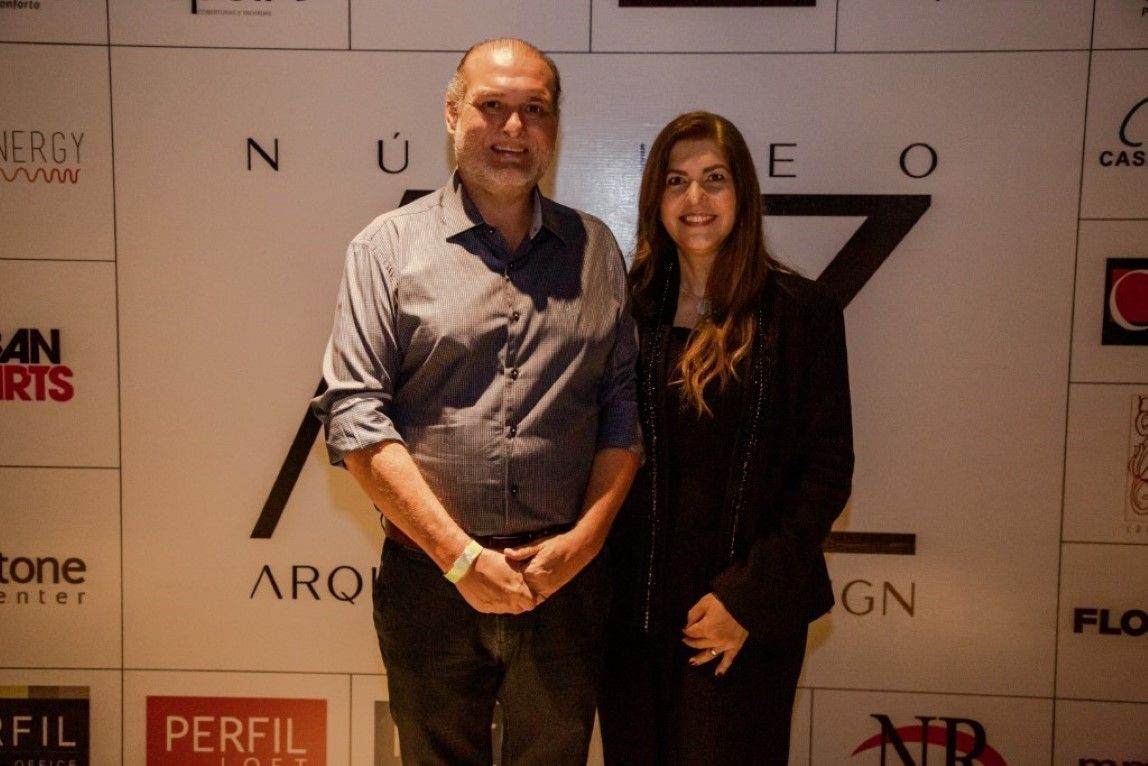 Um homem e uma mulher em pé em frente a uma parede com logotipos