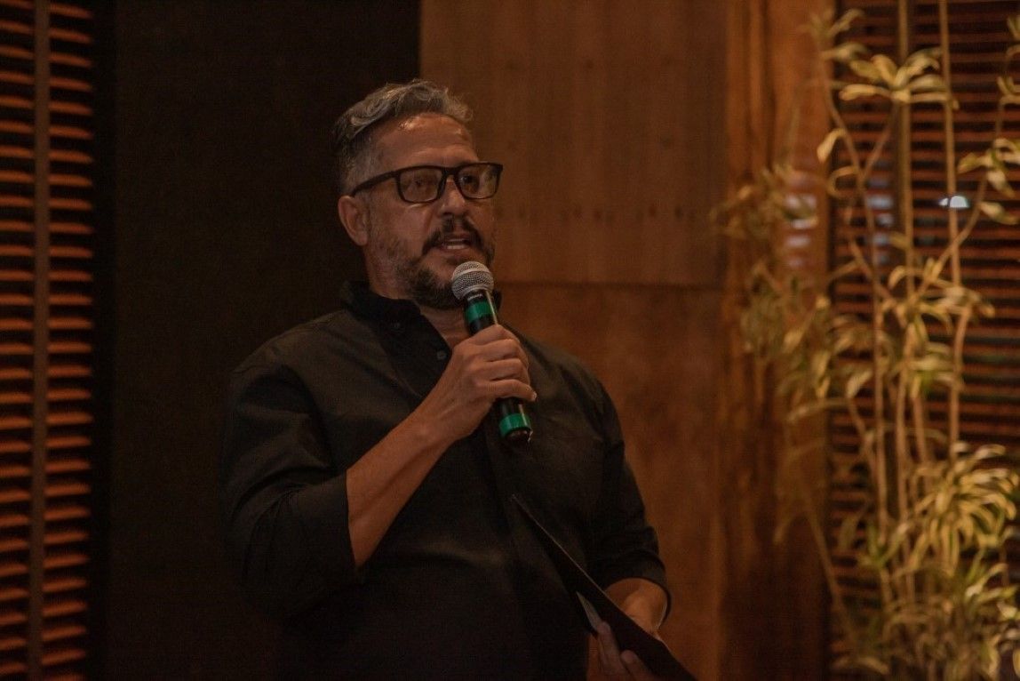 Um homem de óculos segura um microfone na mão.