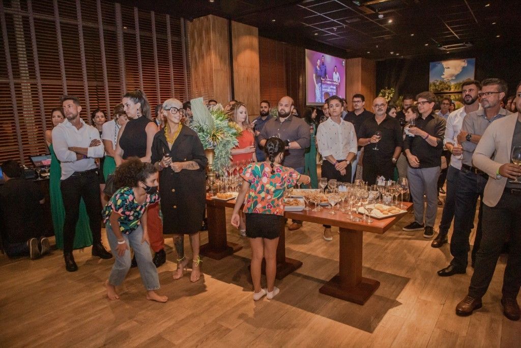 Um grupo de pessoas está de pé ao redor de mesas em uma sala.