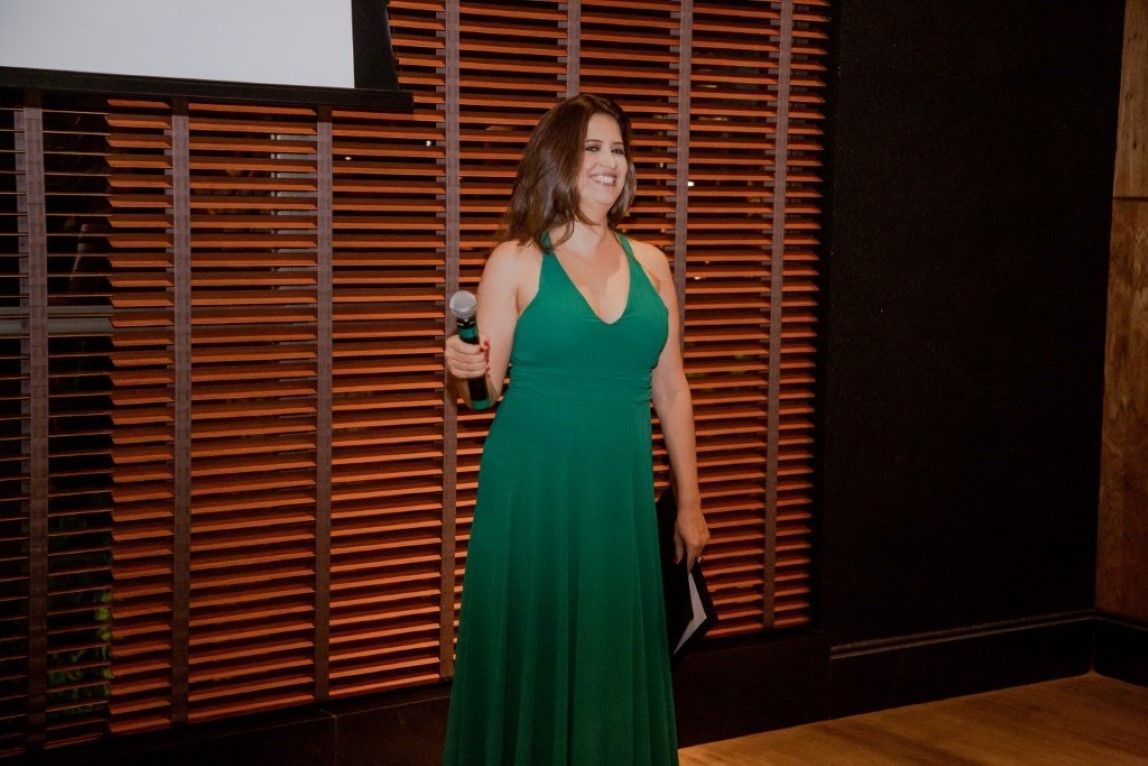 Uma mulher com um vestido verde está parada em frente a uma parede de madeira segurando um microfone.