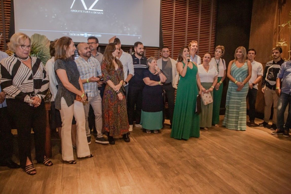 Um grupo de pessoas está de pé sobre um piso de madeira em frente a uma tela grande.