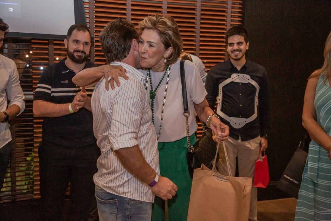 Um homem está abraçando uma mulher em uma sala com outras pessoas.