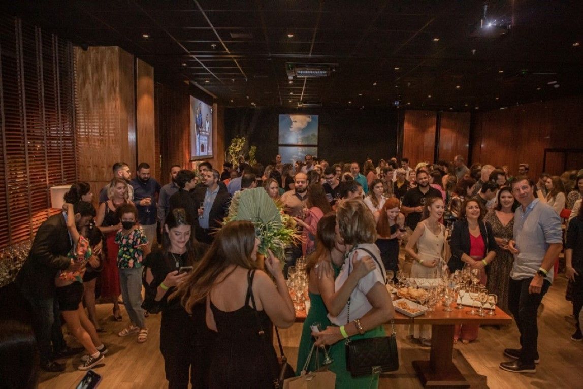 Um grande grupo de pessoas está em pé ao redor de uma mesa em uma sala.