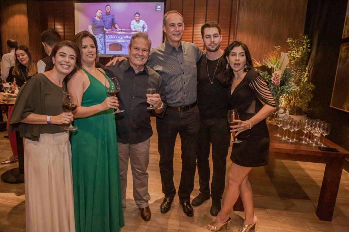 Um grupo de pessoas em pé, uma ao lado da outra, em uma sala, segurando taças de vinho.