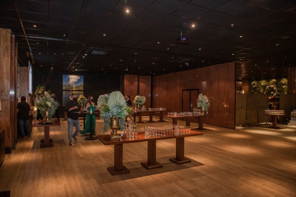 Um grupo de pessoas está de pé ao redor de mesas em uma sala grande.