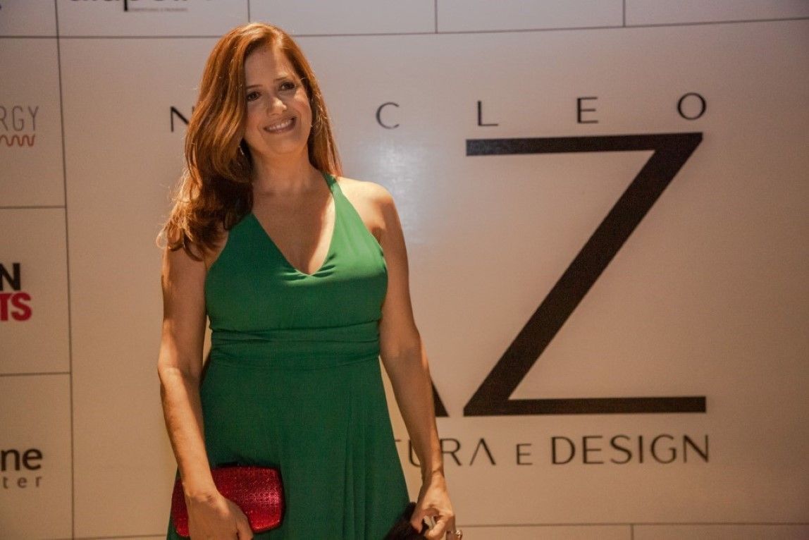 Uma mulher com um vestido verde está parada em frente a uma placa que diz cleo