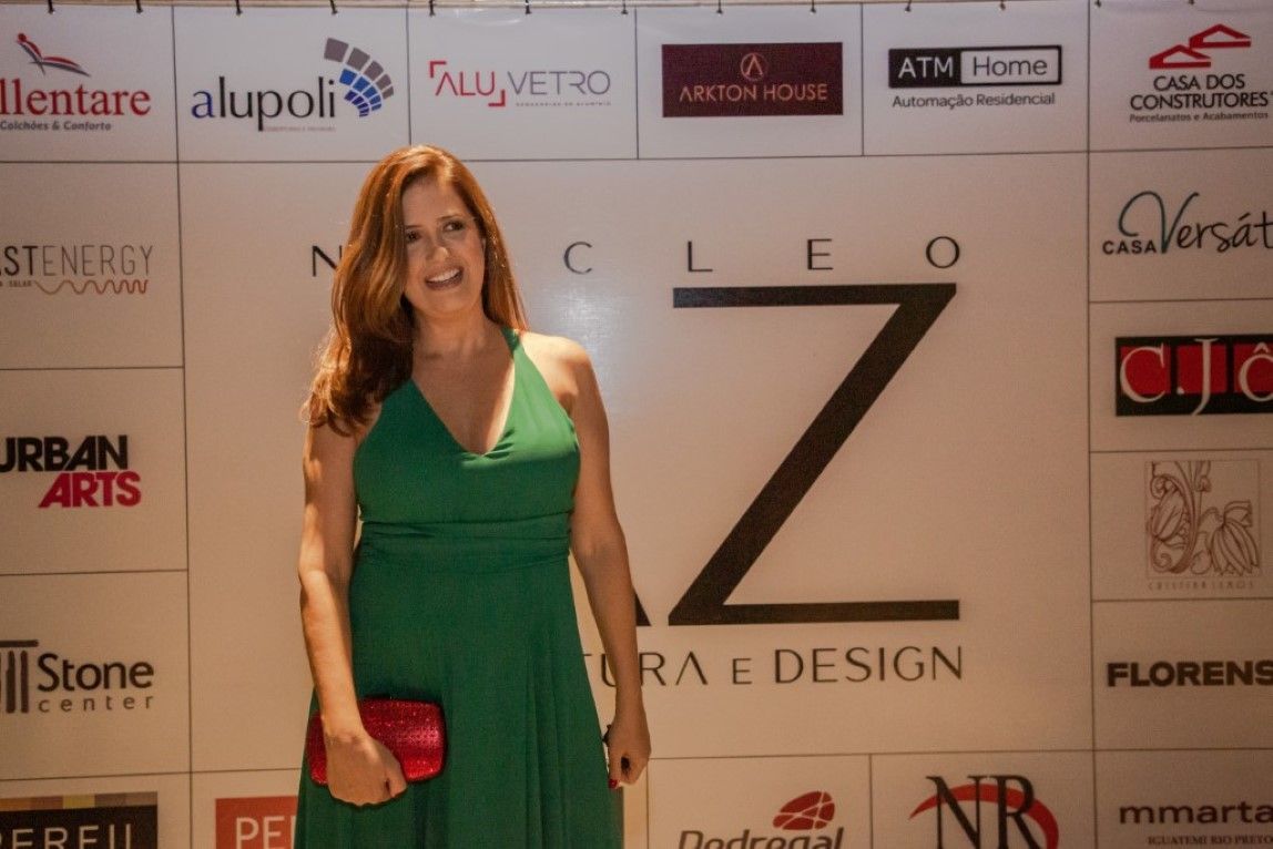 Uma mulher com um vestido verde está em frente a uma parede com logotipos