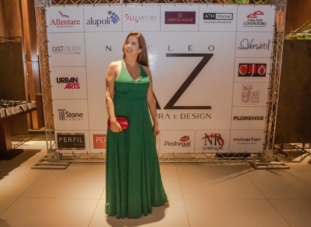 Uma mulher com um vestido verde está parada em frente a uma parede com logotipos