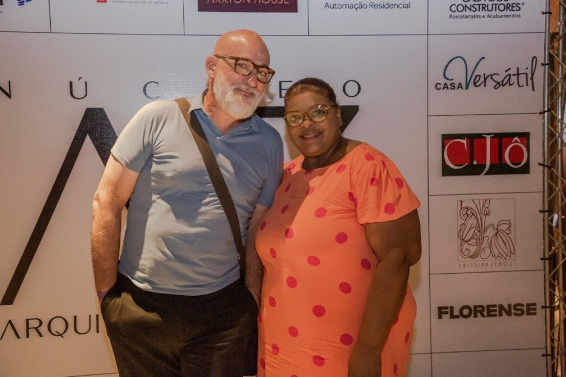 Um homem e uma mulher estão posando para uma foto em frente a uma parede com logotipos.