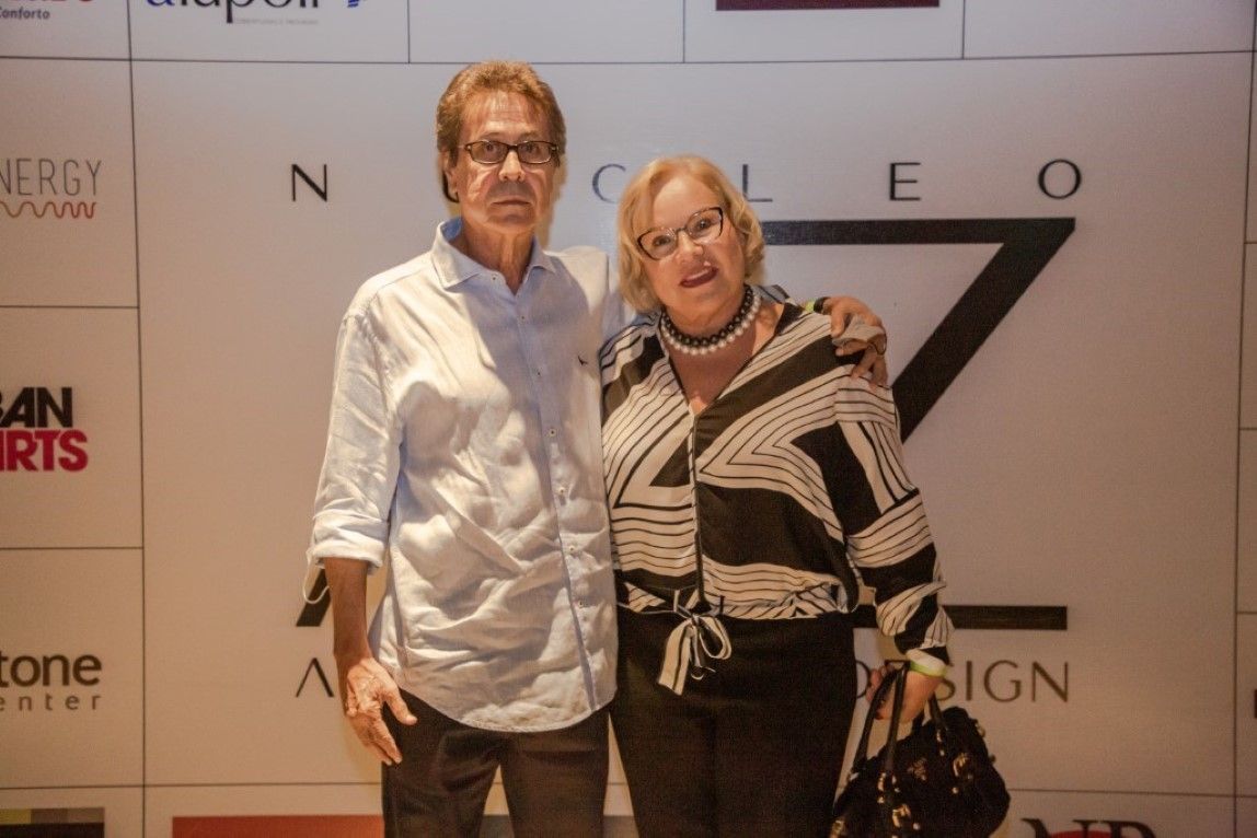 Um homem e uma mulher estão posando para uma foto em frente a uma parede.