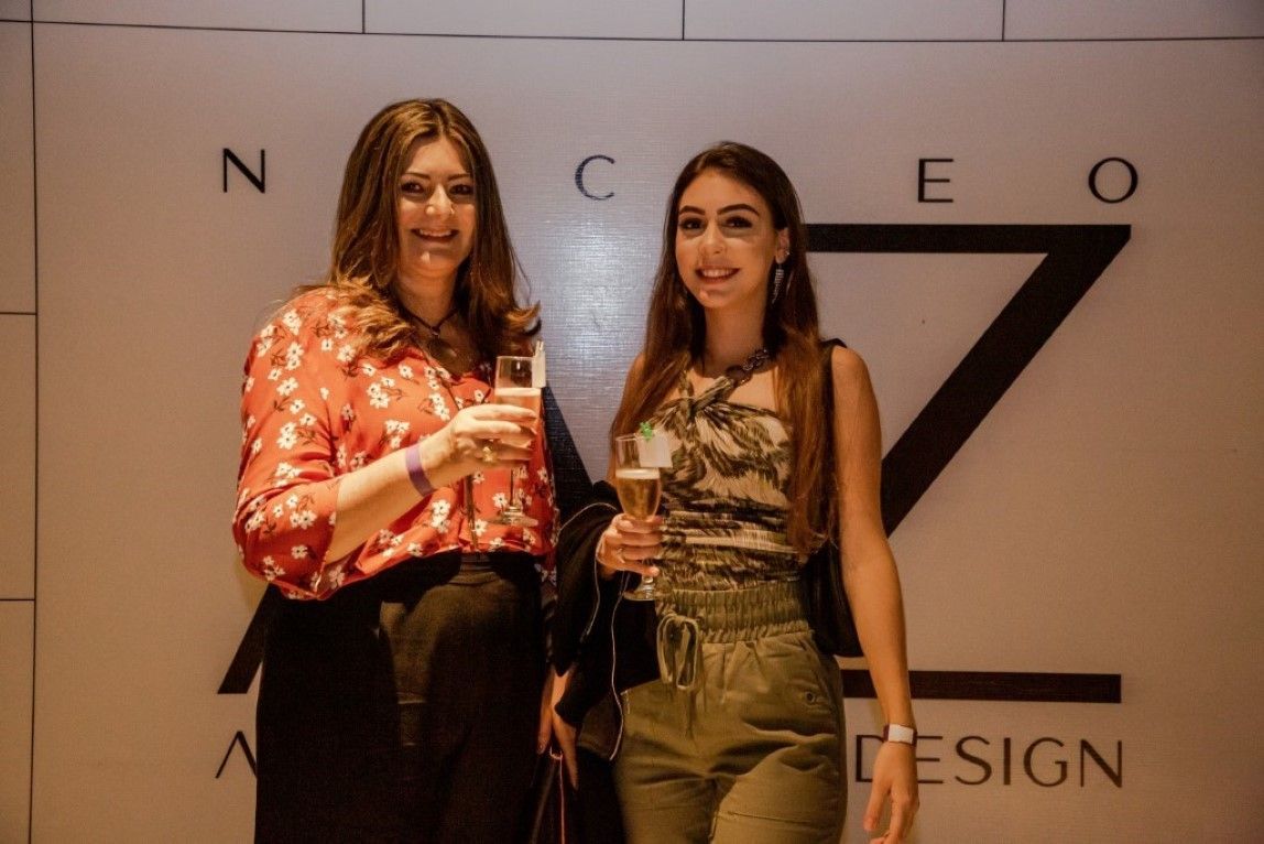 Duas mulheres estão de pé, uma ao lado da outra, em frente a uma placa que diz design.