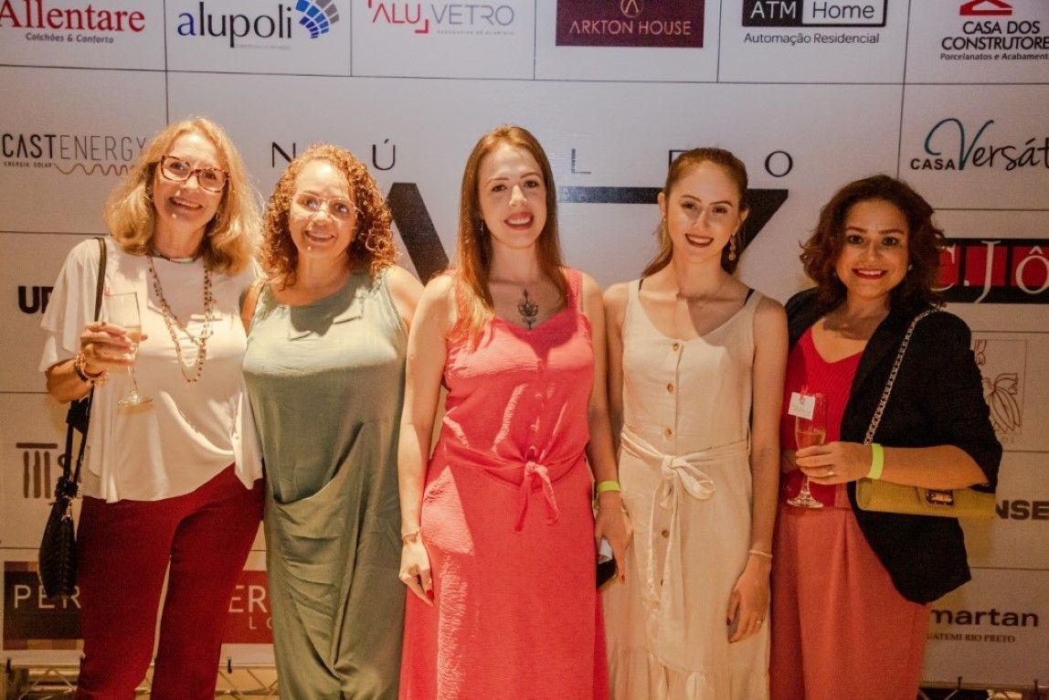 Um grupo de mulheres está posando para uma foto em frente a uma parede com logotipos.