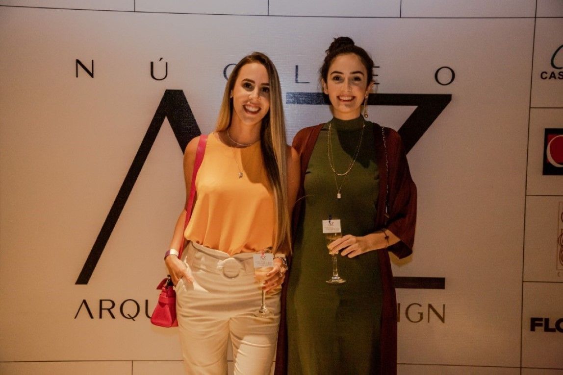 Duas mulheres estão posando para uma foto em frente a uma parede.