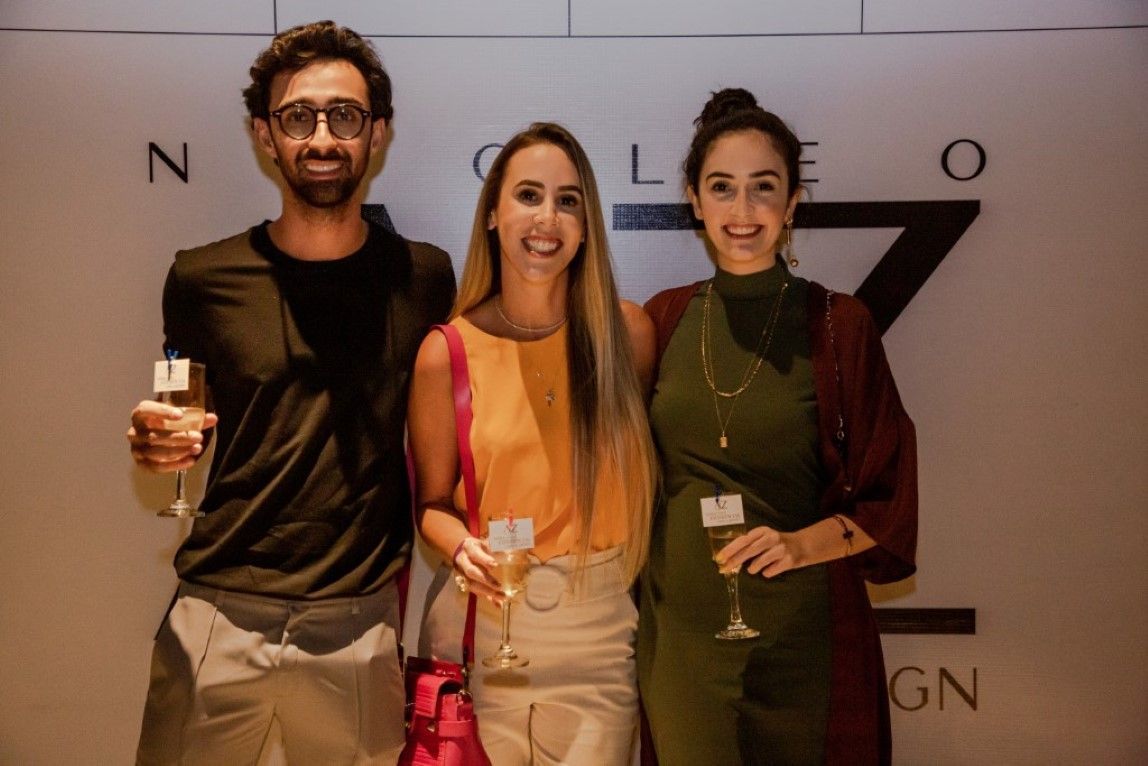 Um homem e duas mulheres estão de pé, um ao lado do outro, segurando taças de vinho.