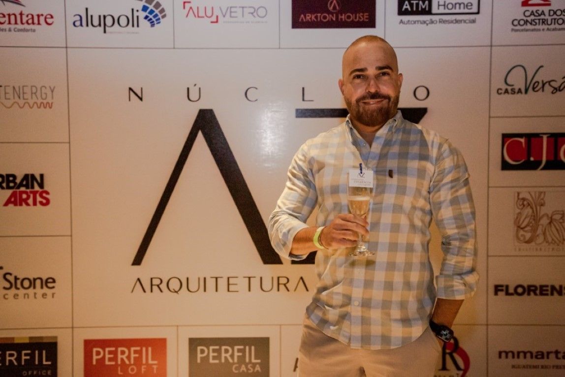 Um homem está segurando uma taça de champanhe em frente a uma parede com logotipos.