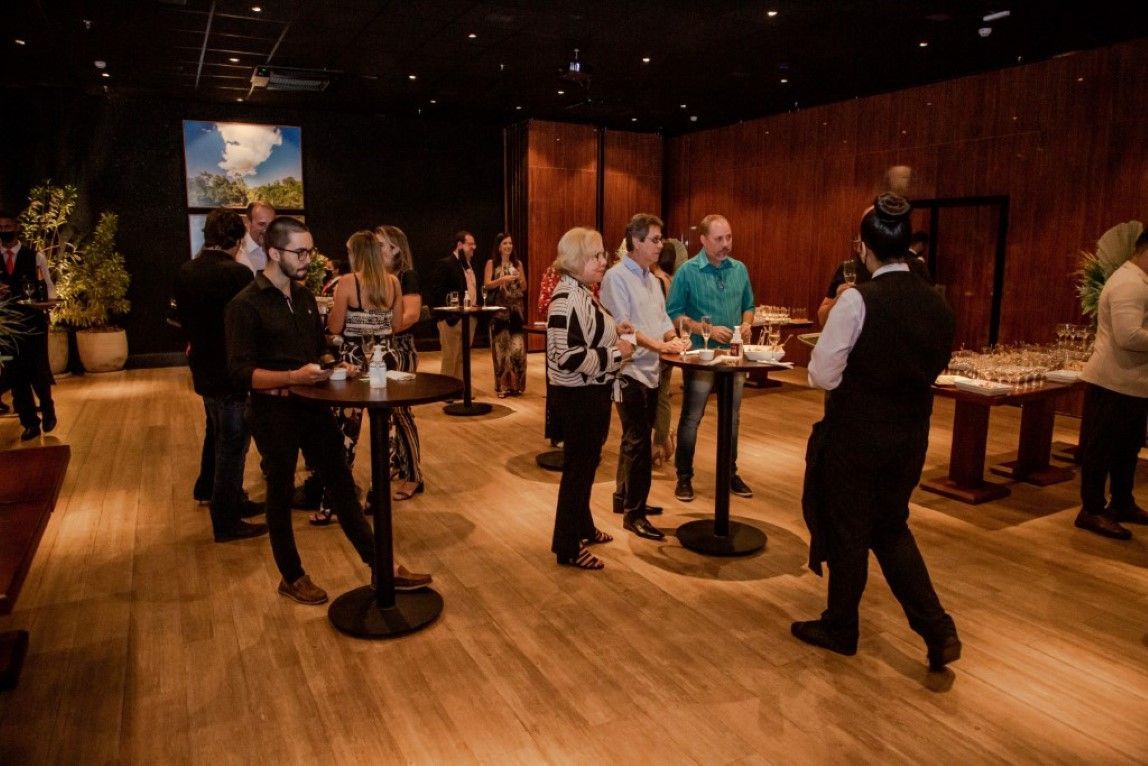 Um grupo de pessoas está de pé ao redor de mesas em uma sala.
