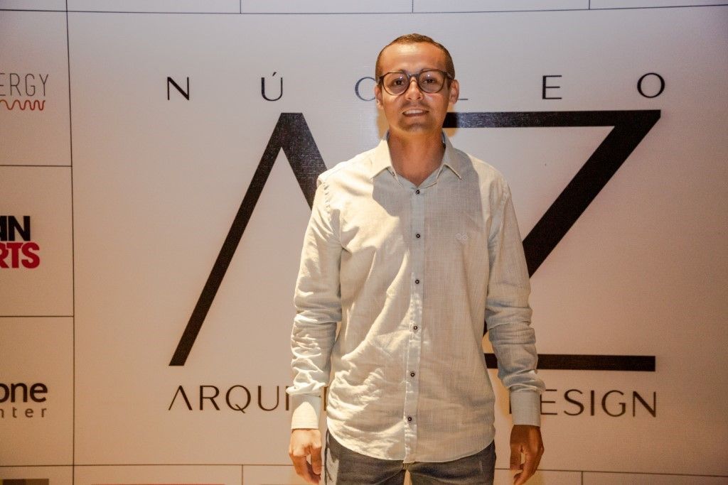 Um homem de óculos e camisa branca está parado em frente a uma placa que diz arquitetura